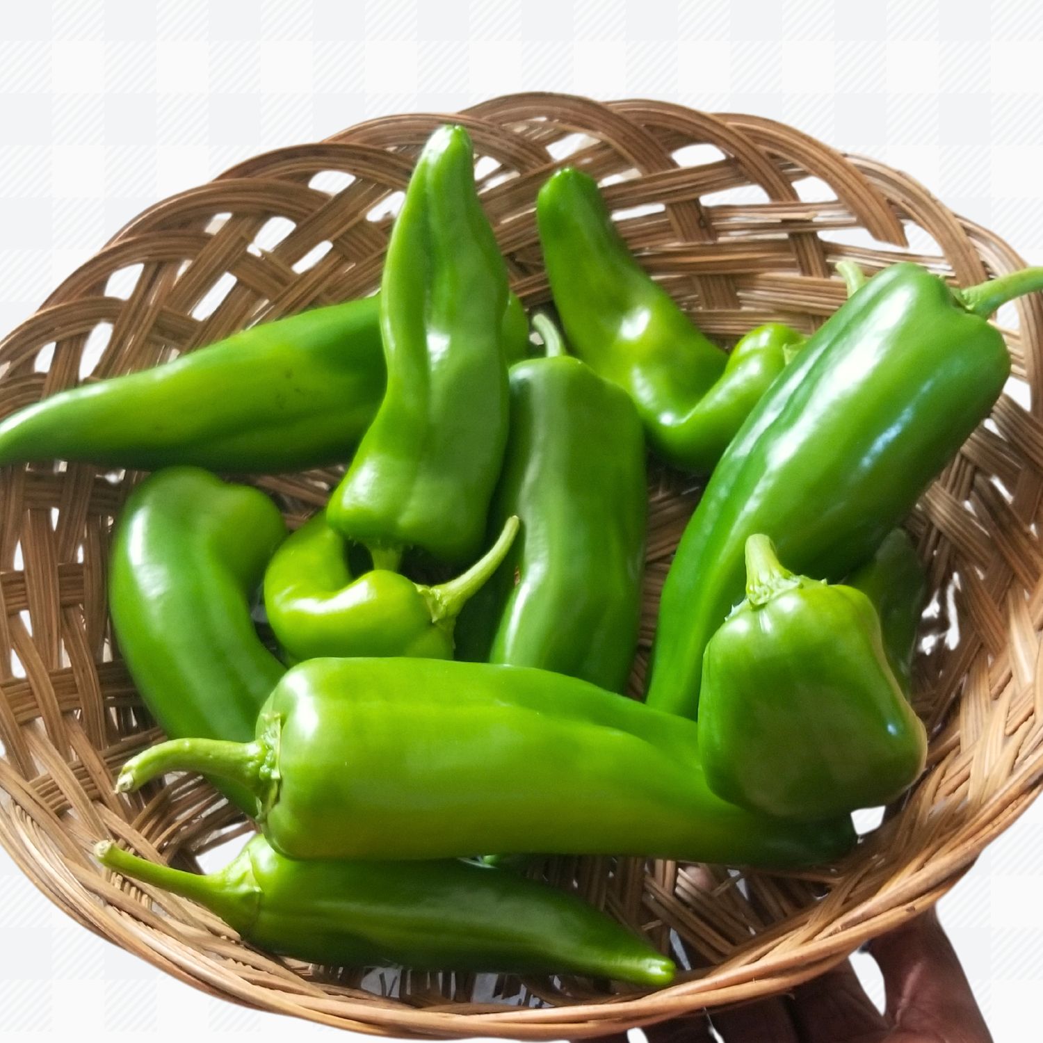 Green banana peppers in brown weaving basket held in a palm